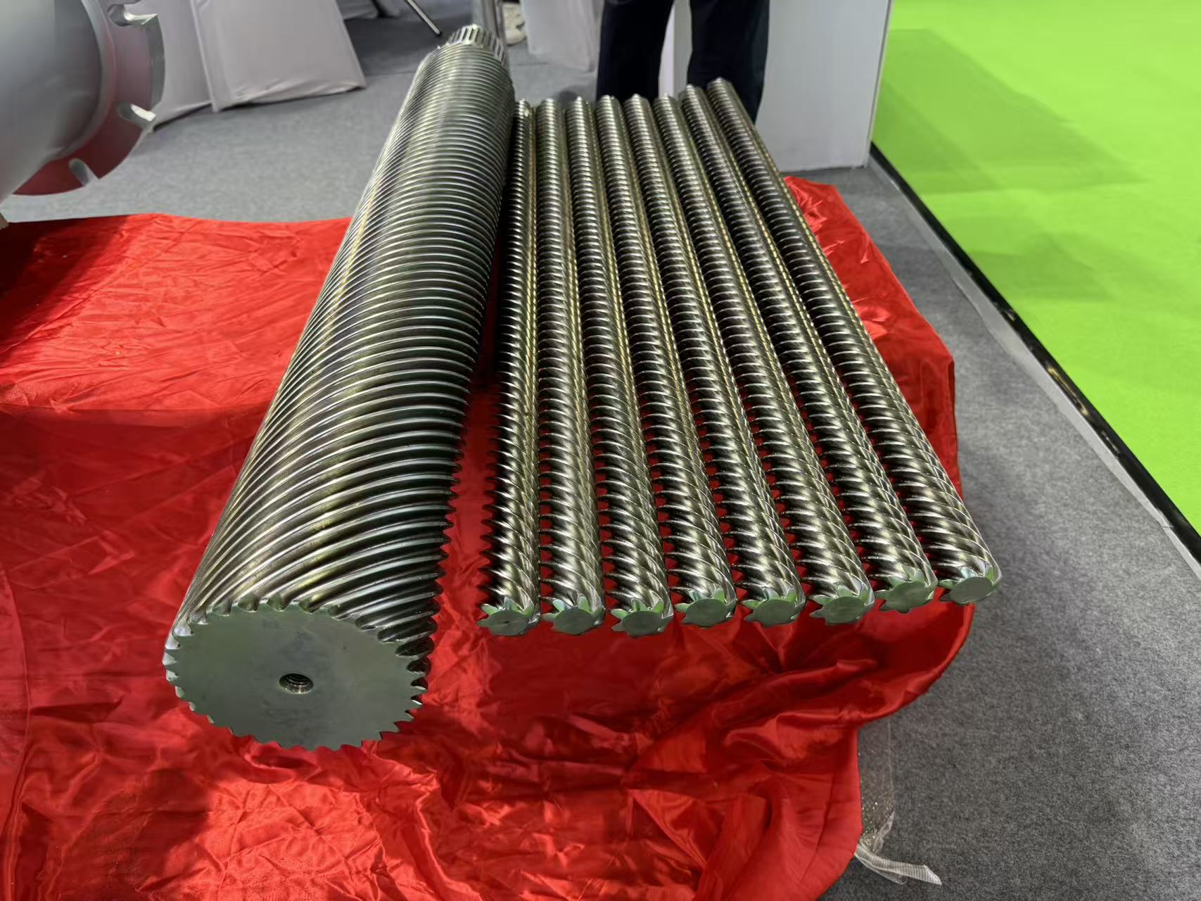 Multiple precision parallel screw barrel assemblies displayed at WB Microwave Machine exhibition booth, showing fine helical thread profile and polished surface finish across different diameter specifications